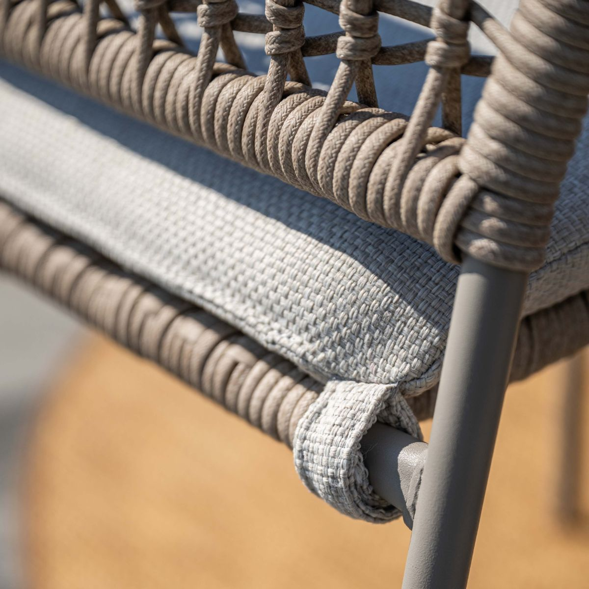 Close-up van een grijs stoelframe met gevlochten touw en kussens.
