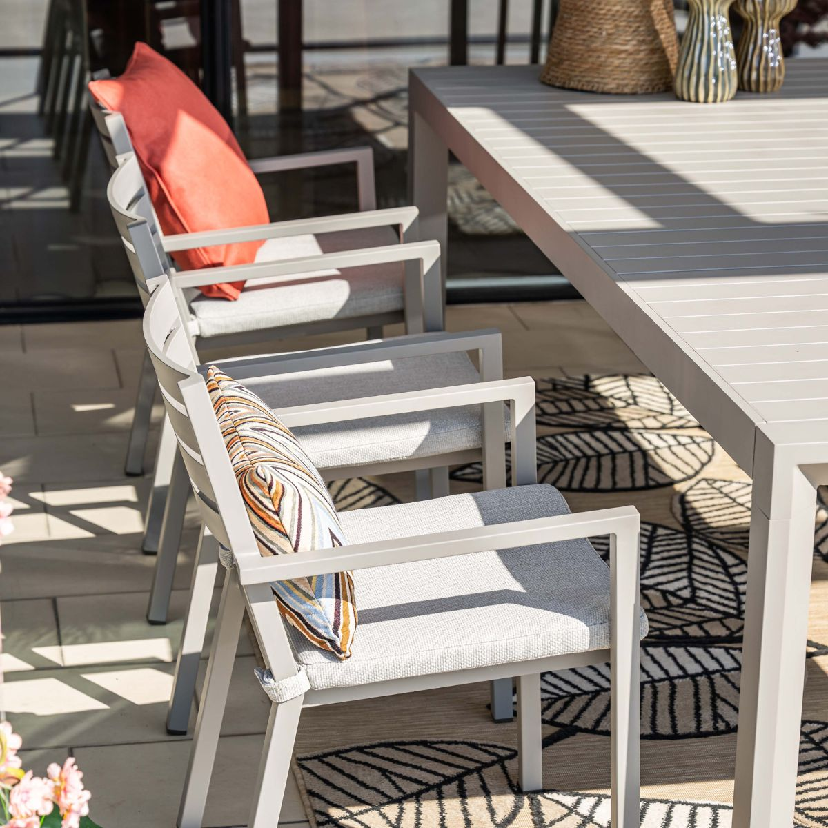 Grijze buitenmeubelen: tafel en stoelen met kussens op een kleed.