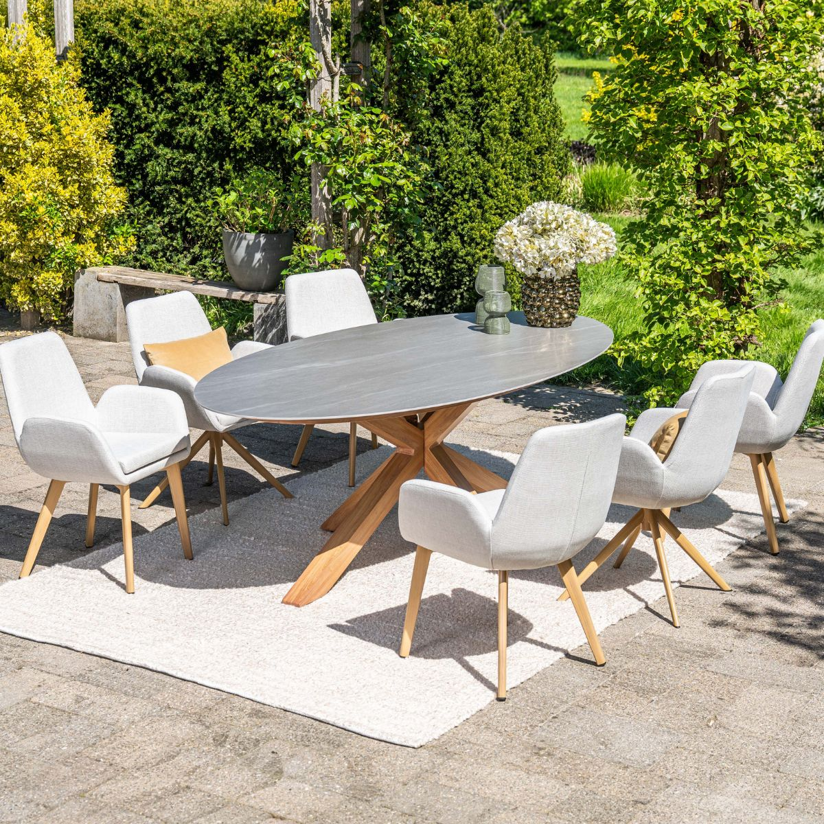 Buiten eethoek met ovale tafel en stoelen op een kleed, omgeven door groen.