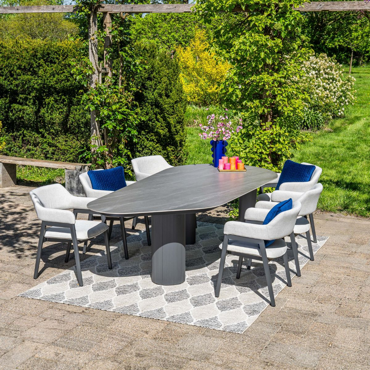 Een ovale tafel met zes stoelen in een tuin op een vloerkleed met patroon.