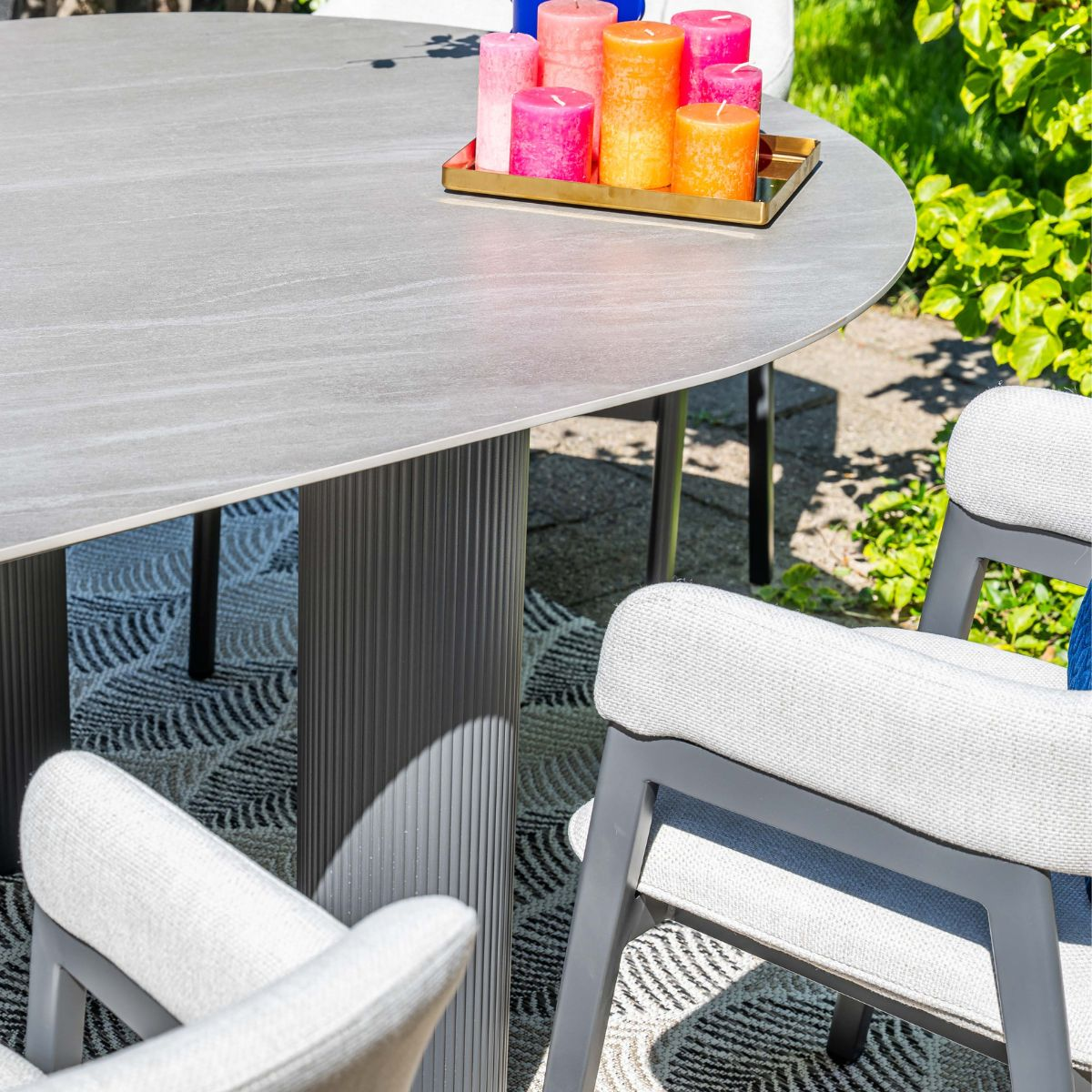 Grijze buitentafel met stoelen, kaarsen op een dienblad en planten.