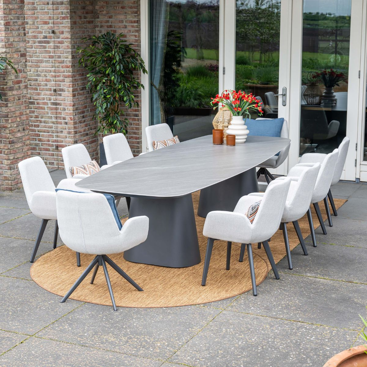 Een grijze eettafel met acht witte stoelen op een ronde buitenmat.