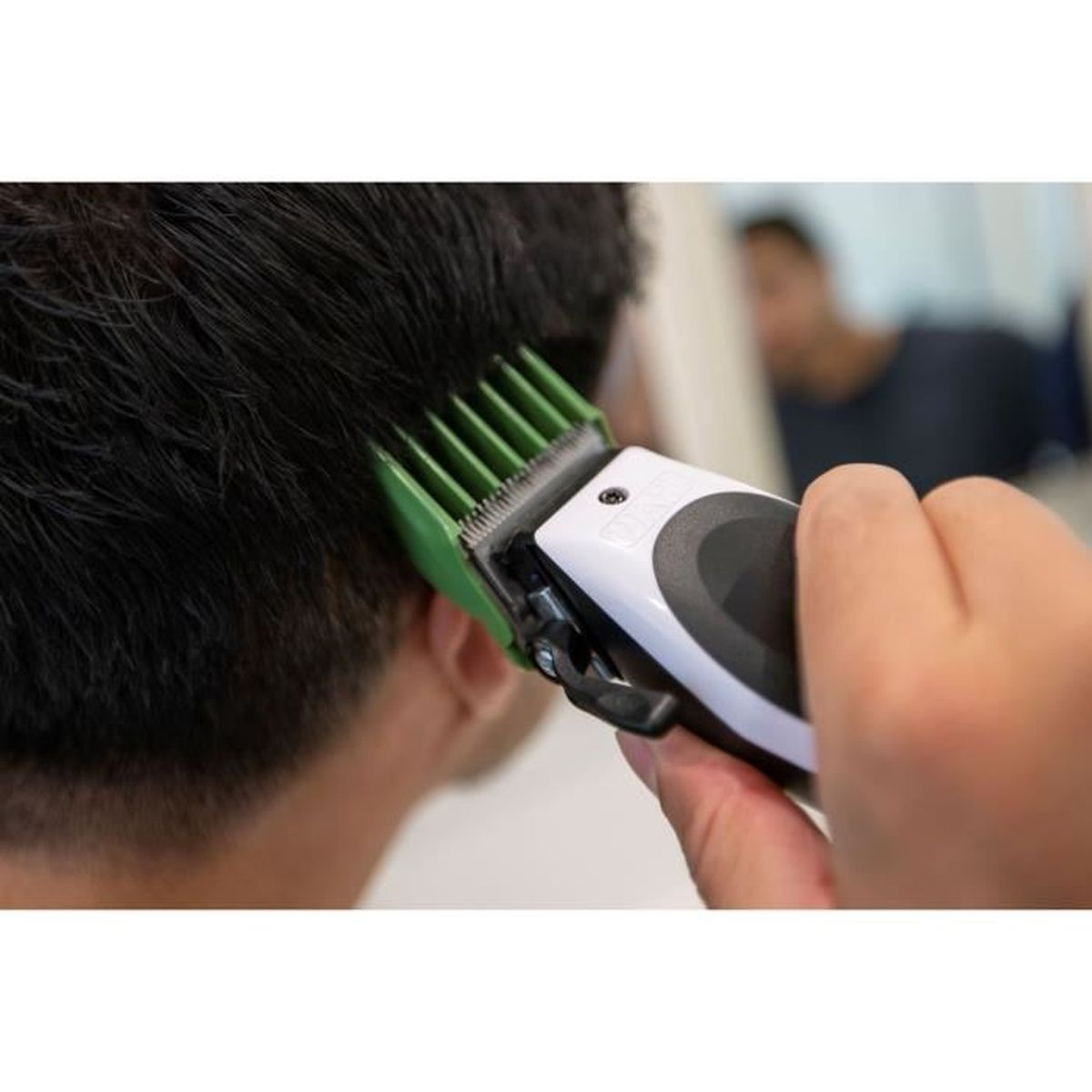 Ręka używa maszynki do włosów z zieloną nakładką na ciemnych włosach.