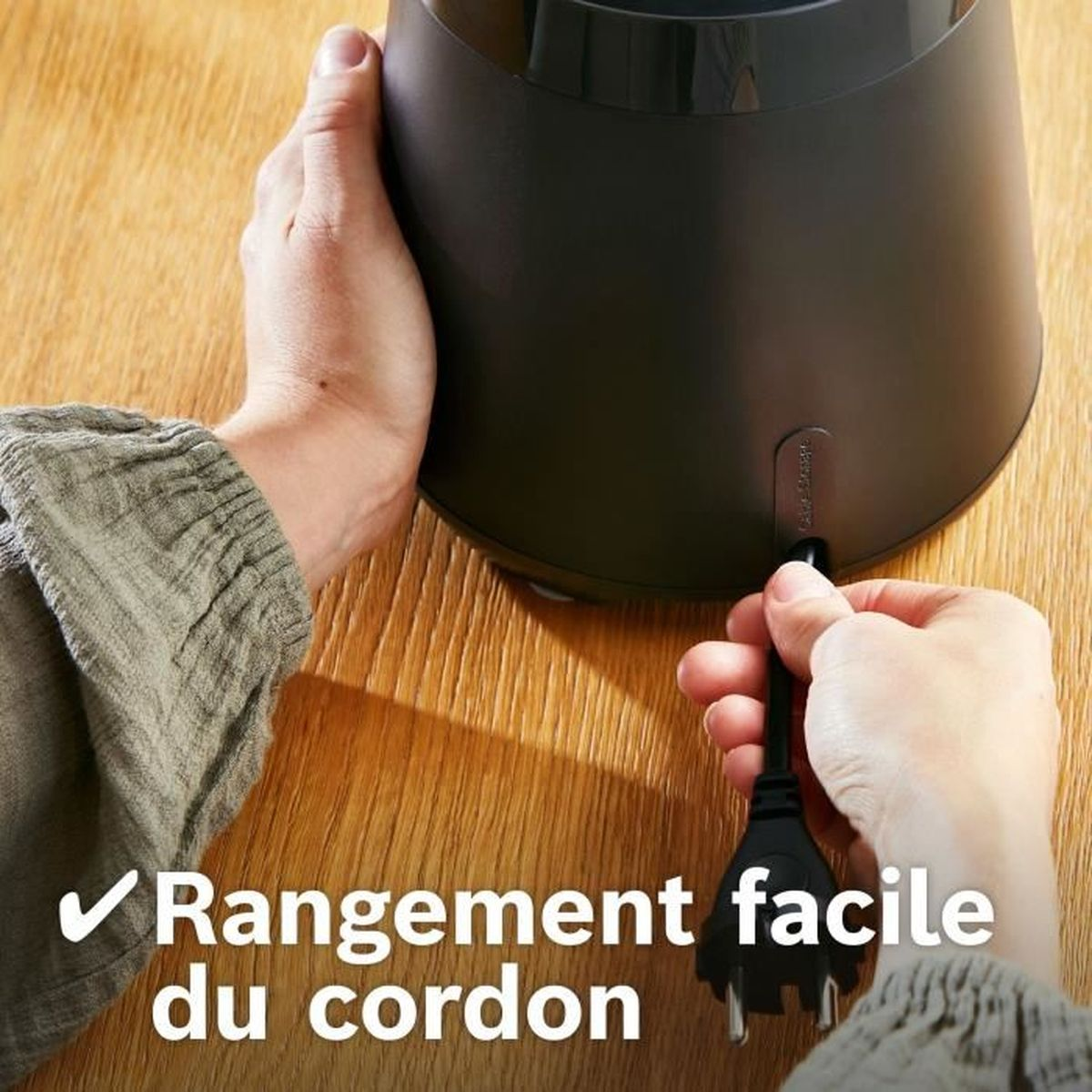 Una mano inserisce un cavo nero in un dispositivo nero su un tavolo di legno.