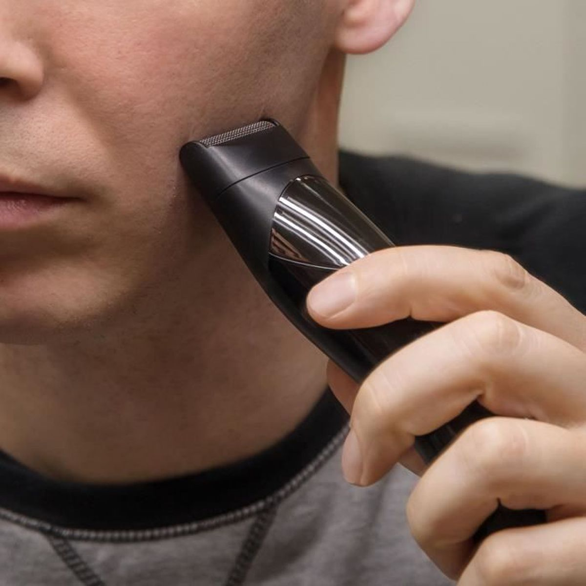 Mann trimmt seinen Bart mit einem schwarzen Trimmer am Kinn.