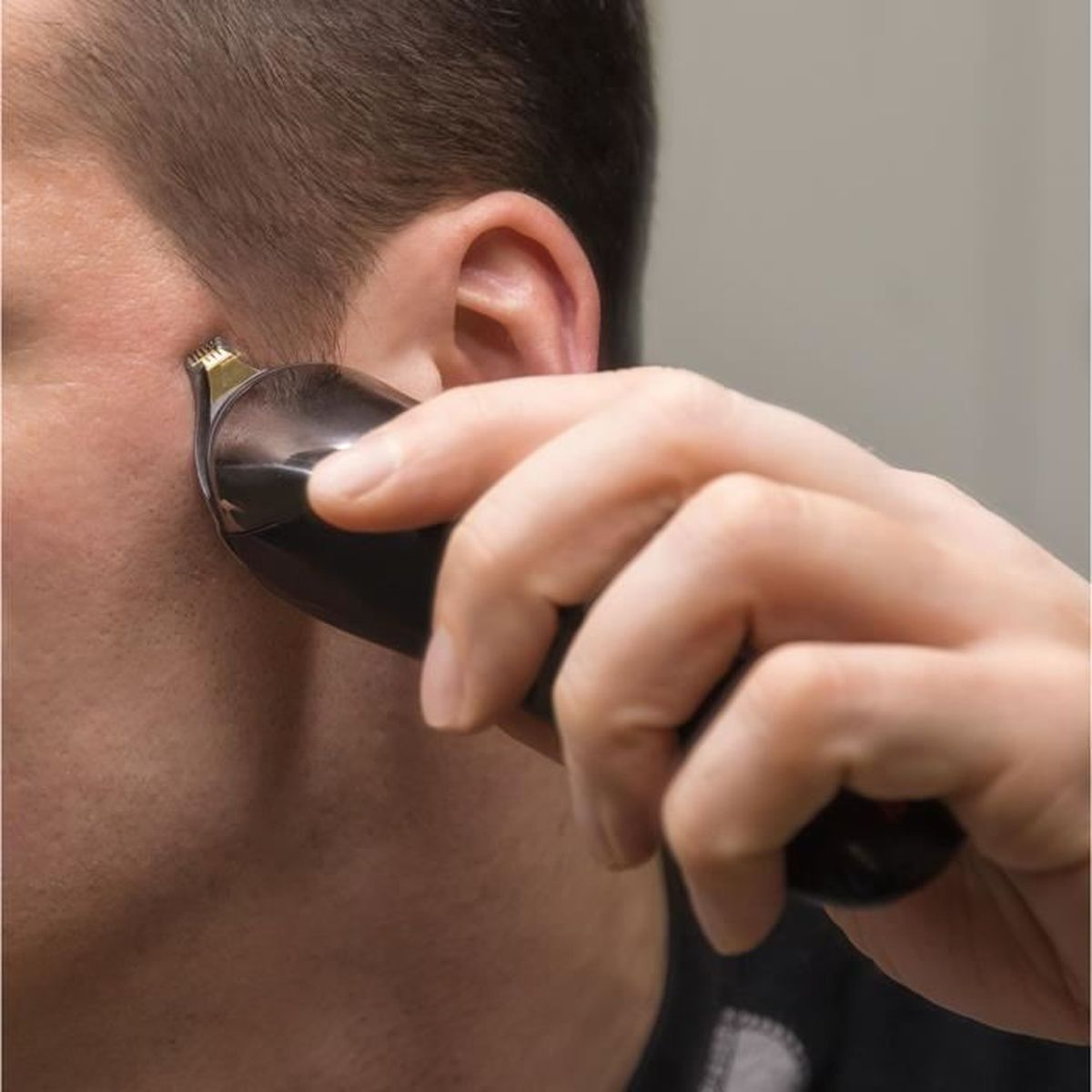 Nahaufnahme einer Hand, die einen schwarzen Trimmer am Gesicht einer Person benutzt.