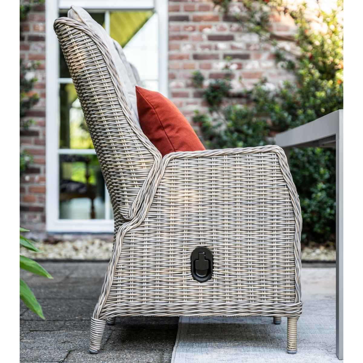 Rieten fauteuil met rood kussen en handvat aan de zijkant.