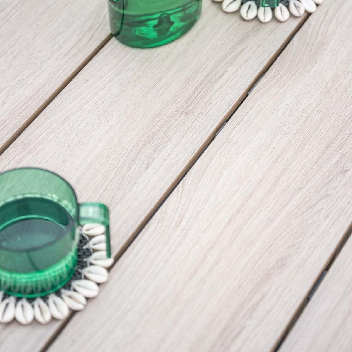 Twee groene glazen staan op schelp onderzetters op een houten tafel.
