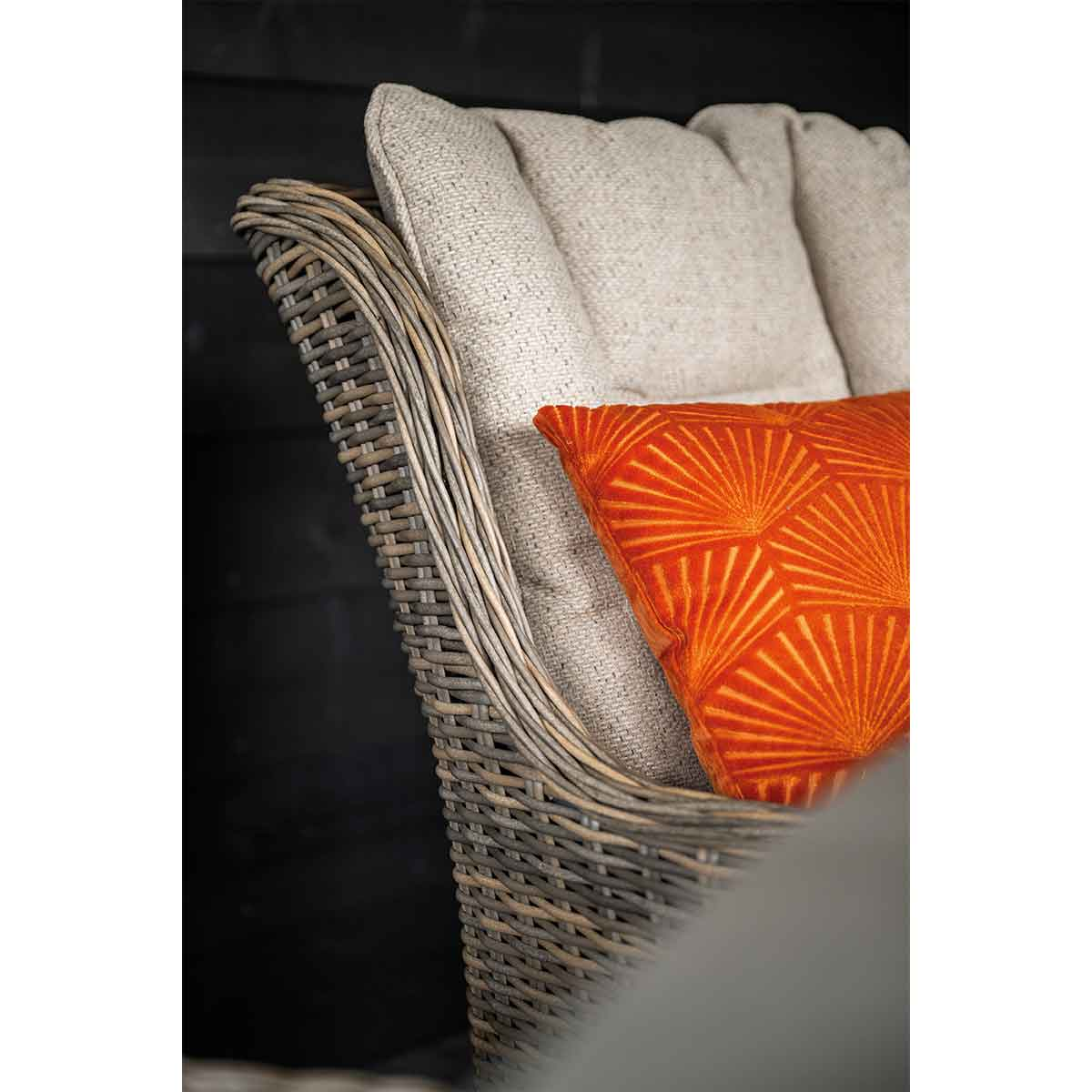 Rieten stoel met lichtgrijze kussens en een oranje kussen met patroon.