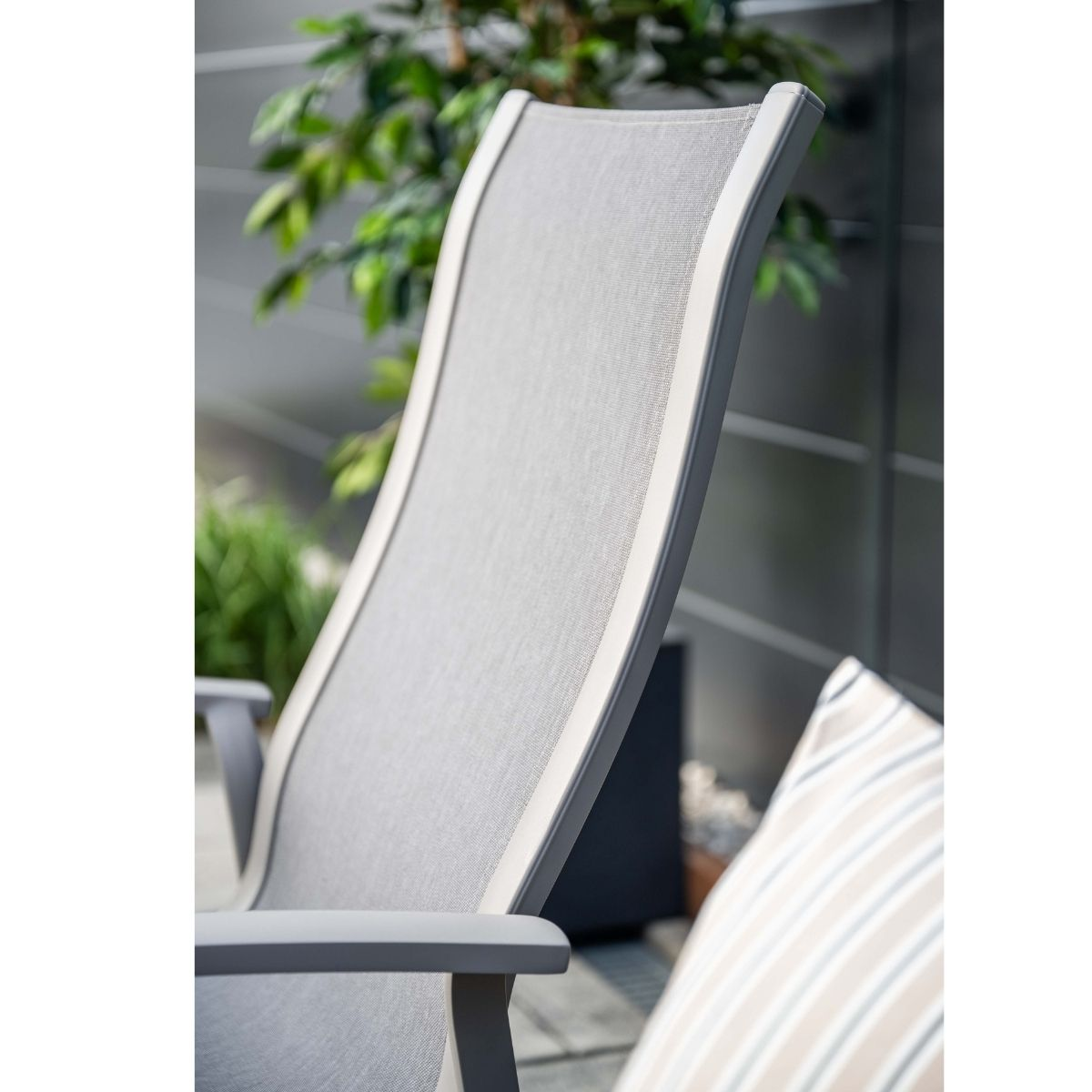 Grijze loungestoel met zilveren frame en kussen. Buiten met groen.