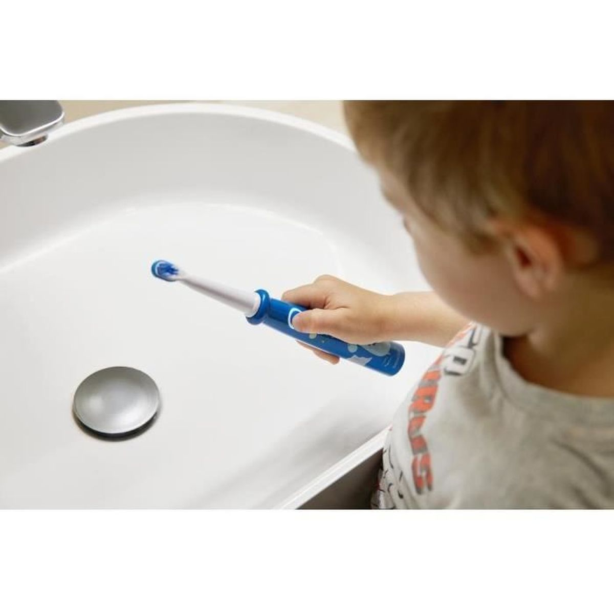 Ein Kind hält eine blaue Zahnbürste über einem weißen Waschbecken.