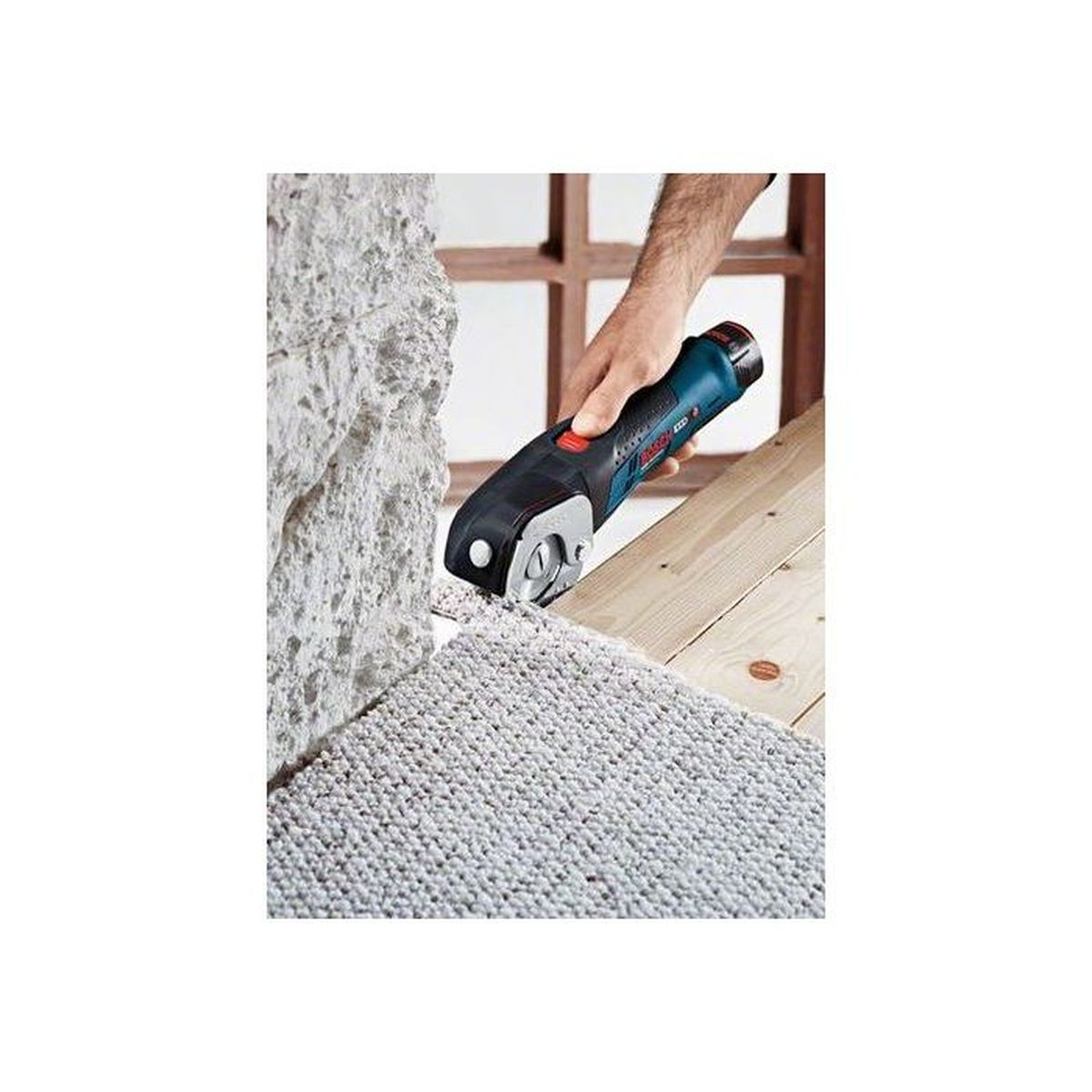 Mężczyzna używa niebiesko-czarnej przecinarki Bosch do cięcia dywanu.