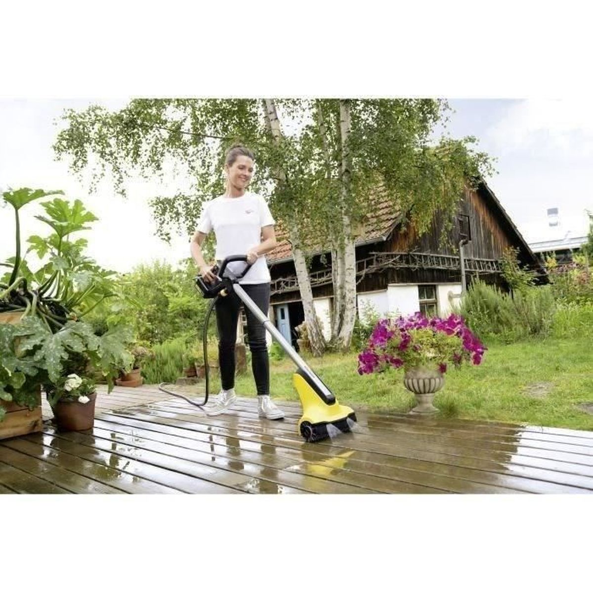 Frau reinigt Holzdeck mit einem gelben Reinigungsgerät im Garten.