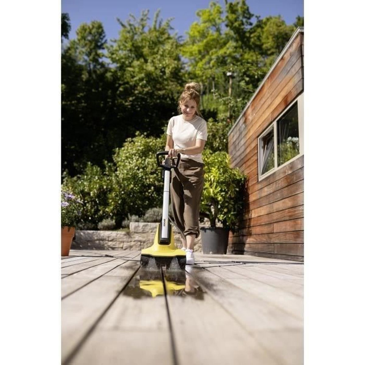 Eine Frau reinigt eine Holzterrasse mit einem gelben Bodenreiniger.