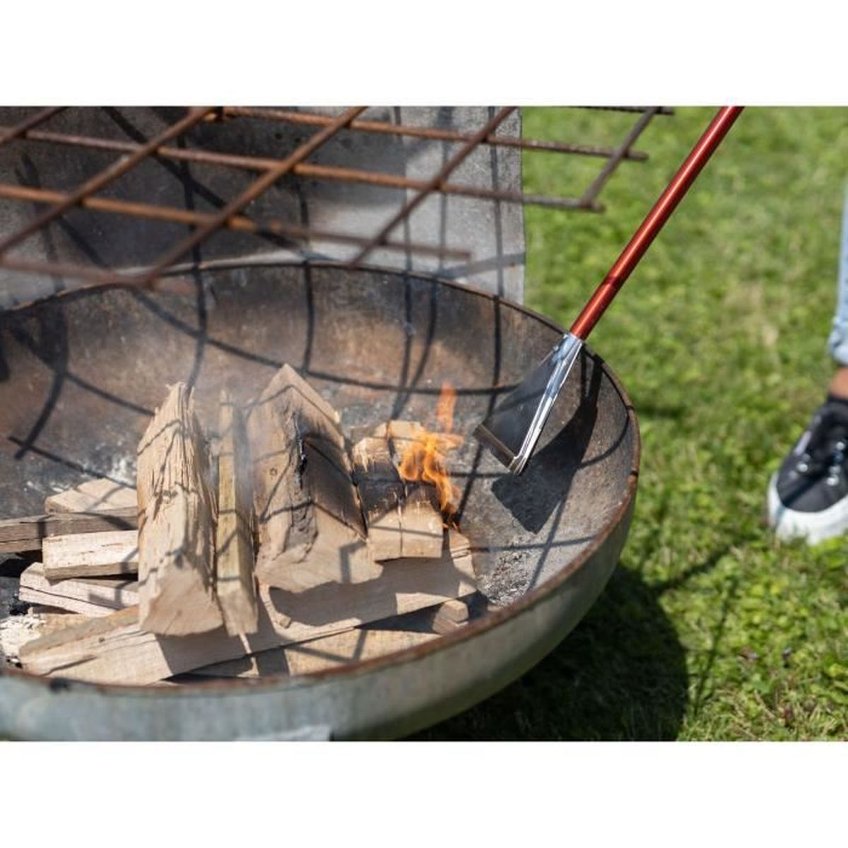 Ein Schürhaken schürt Holz in einer Feuerschale auf Gras.
