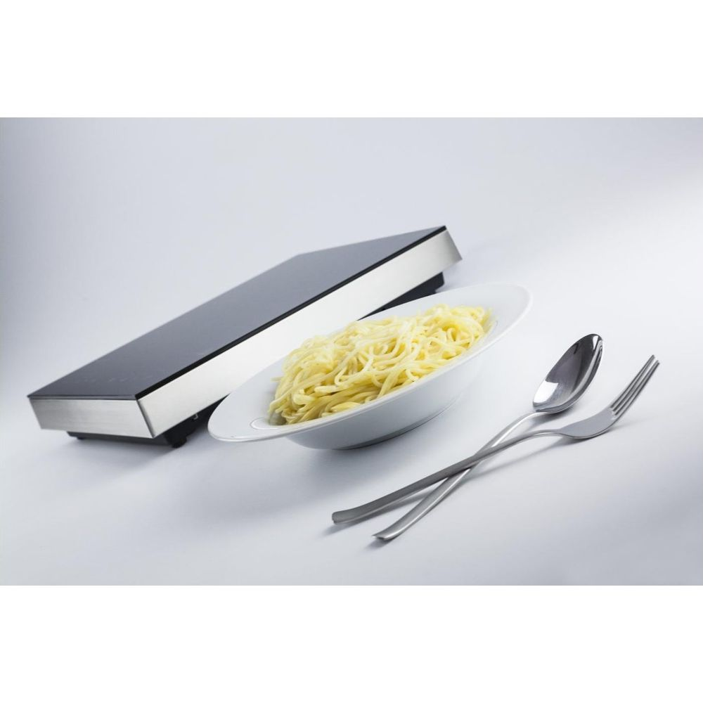 Eine Platte Spaghetti in einer weißen Schüssel neben einem Induktionskochfeld und Besteck.