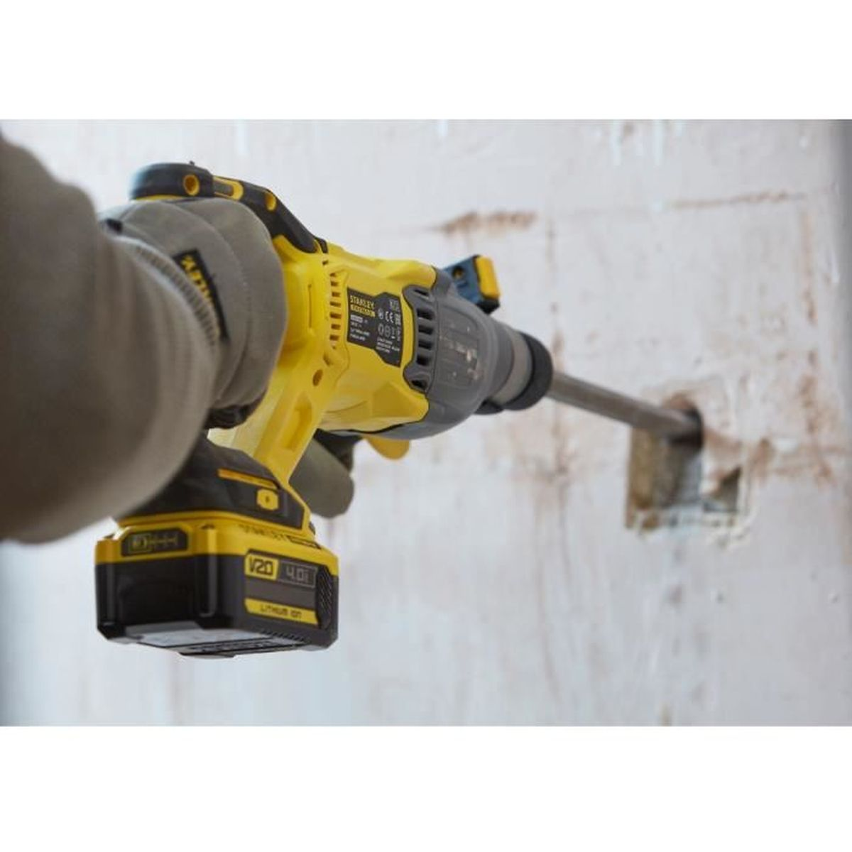 Eine gelbe Bohrmaschine wird von einer Person mit Handschuhen benutzt, um ein Loch in eine weiße Wand zu bohren.
