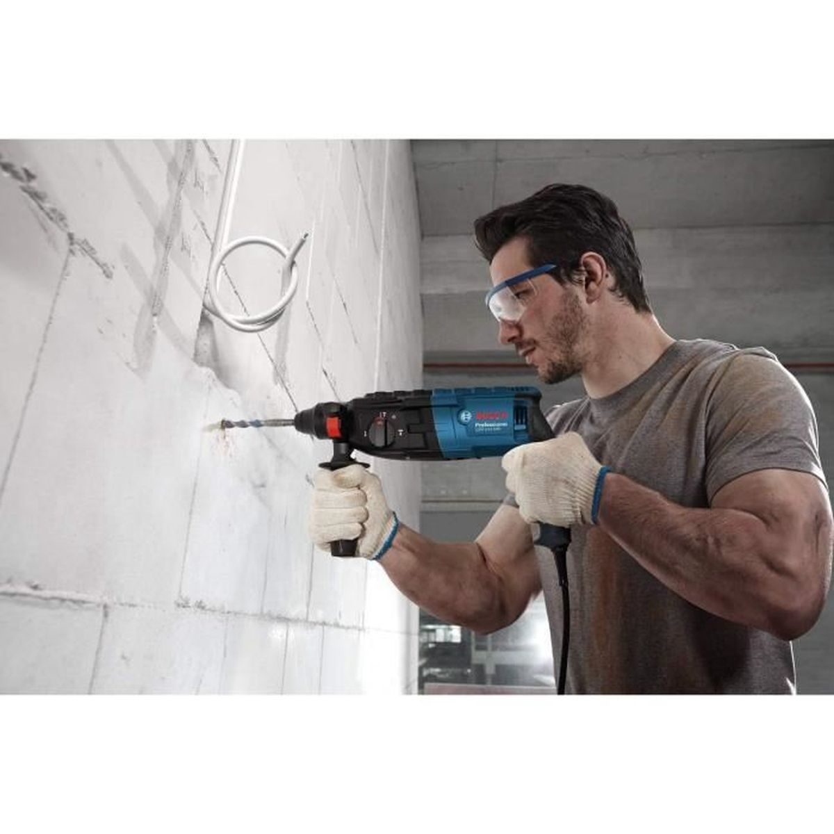 Mann mit Schutzbrille bohrt mit Schlagbohrmaschine in Wand.