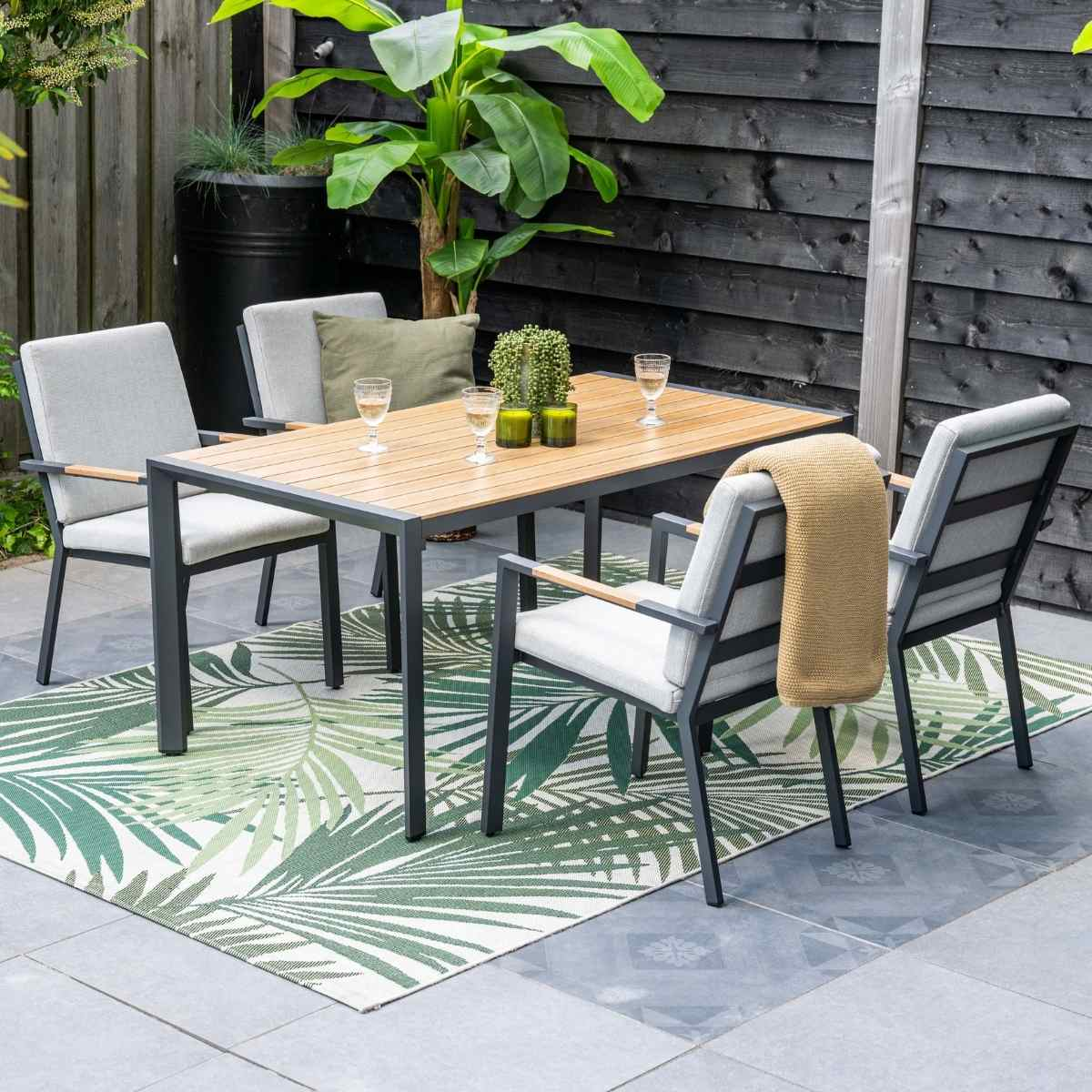 Een tuintafel met vier stoelen, op een vloerkleed met bladerenpatroon.
