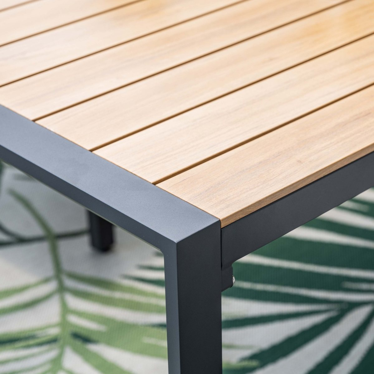Close-up van een houten tafelblad met donker metalen frame op een vloerkleed met bladeren.