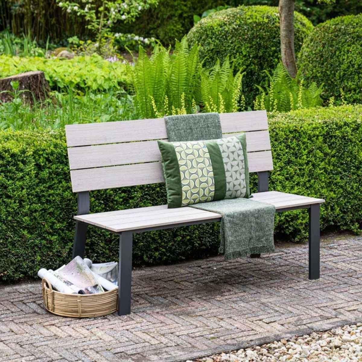 Een tuinbank met kussens en deken in een weelderige tuin.
