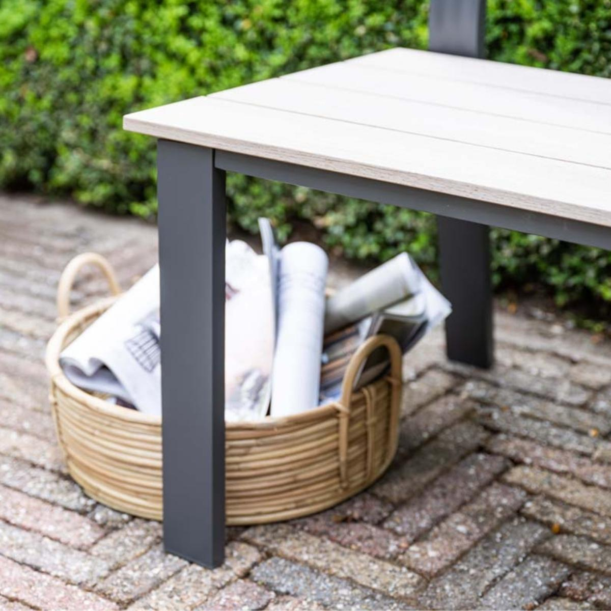 Een rieten mand met kranten onder een tafel op een stenen terras.