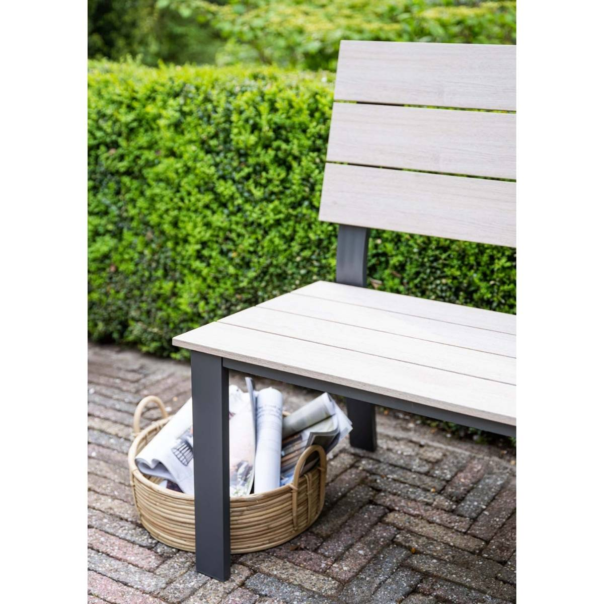Houten bank met metalen frame op een stenen pad met een mand met kranten ernaast.