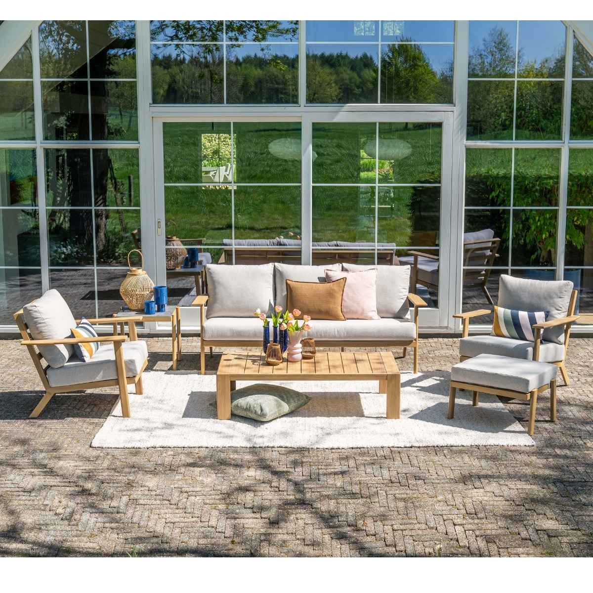 Een tuinmeubelset met bank, stoelen en salontafel op een stenen terras.