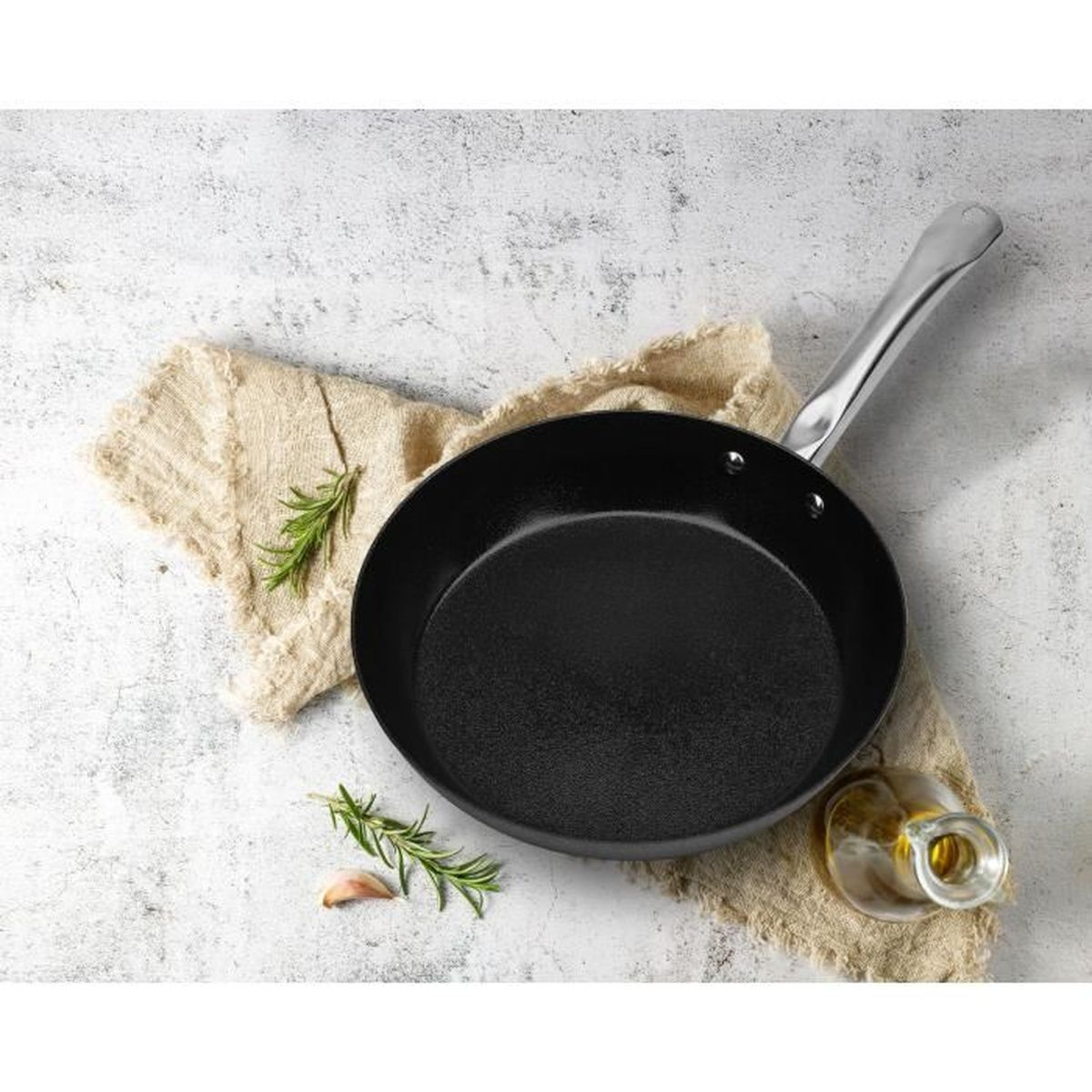 Schwarze Pfanne mit Stiel, darauf ein Leinentuch, Rosmarin und Knoblauch.