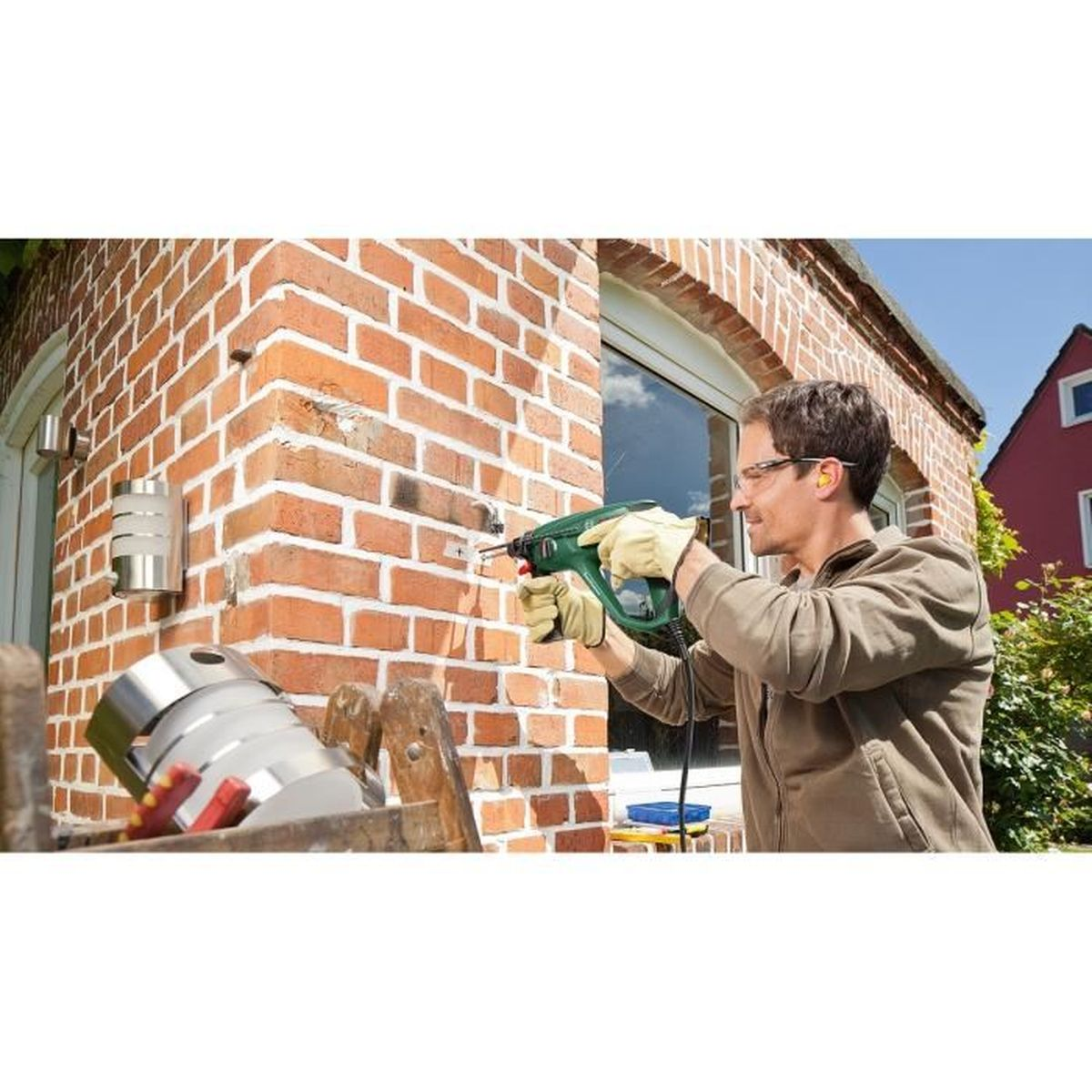 Homme perce un mur de briques, porte gants et lunettes.