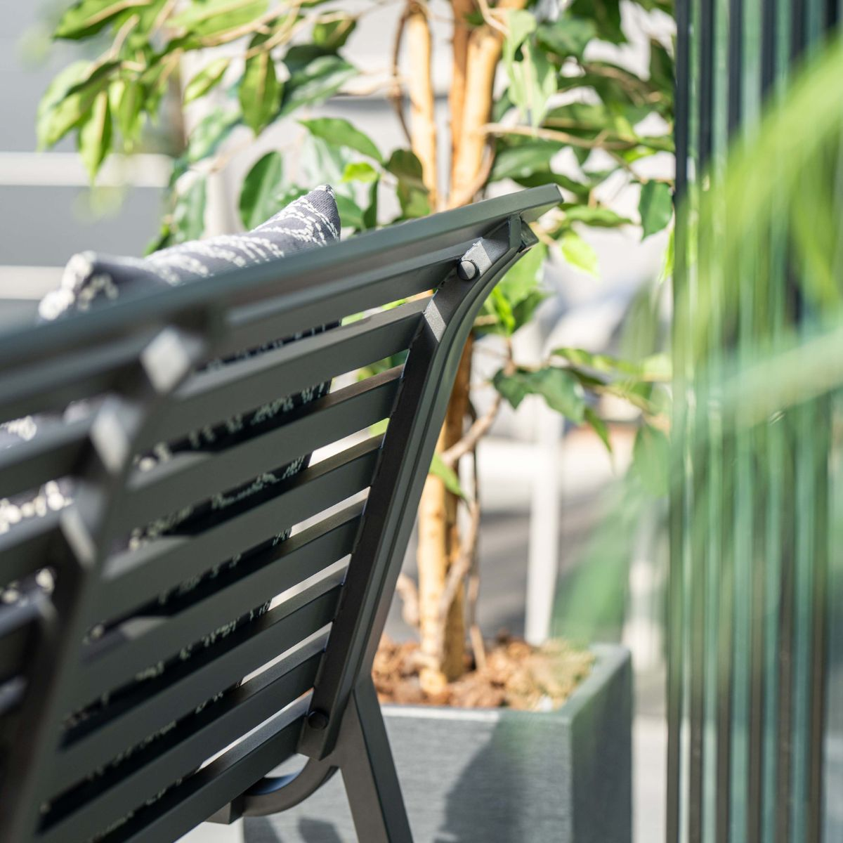 Donkergrijze tuinbank met gestipt kussen, boom in pot.