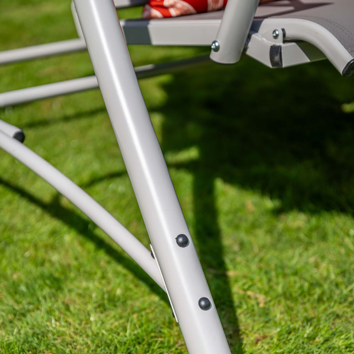 Grijs metalen stoelframe op groen gras met schaduwen.