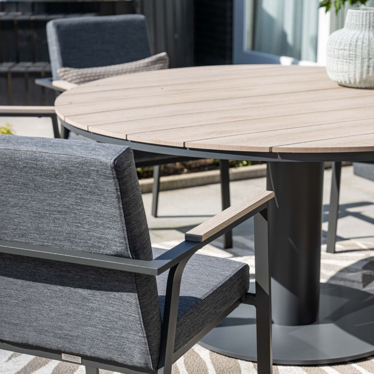 Een ronde houten tafel met grijze stoelen op een patio.