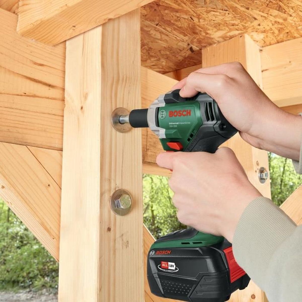 Eine Person benutzt einen grünen Bosch-Akkuschrauber, um eine Schraube in Holz zu drehen.