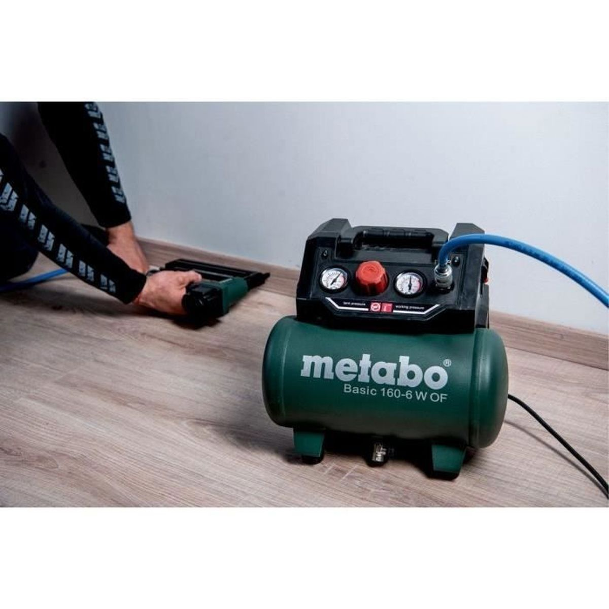 Ein Mann benutzt einen grünen Metabo-Kompressor und einen Nagler auf einem Holzboden.