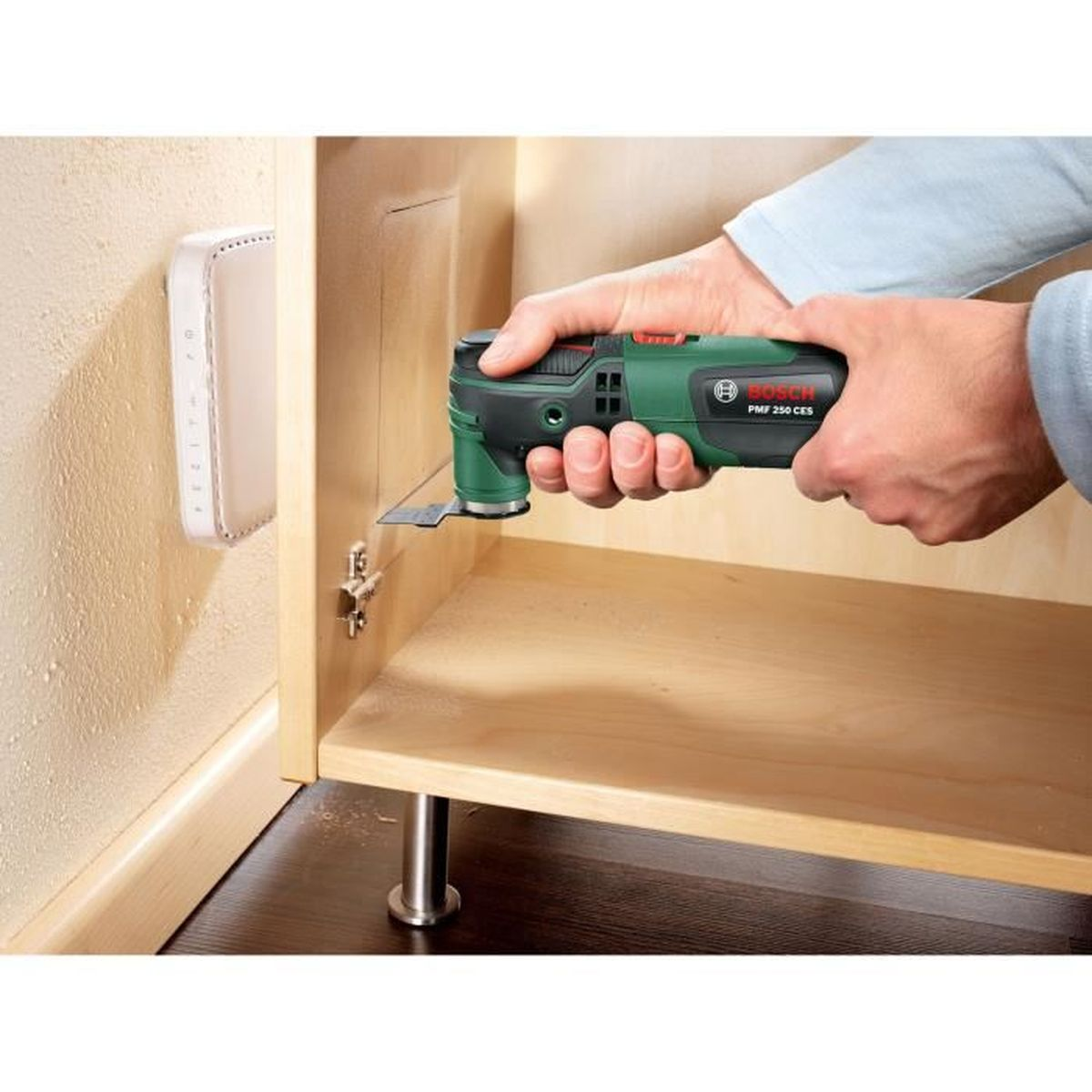 Uomo usa utensile oscillante su mobile in legno; supporto a muro bianco vicino.