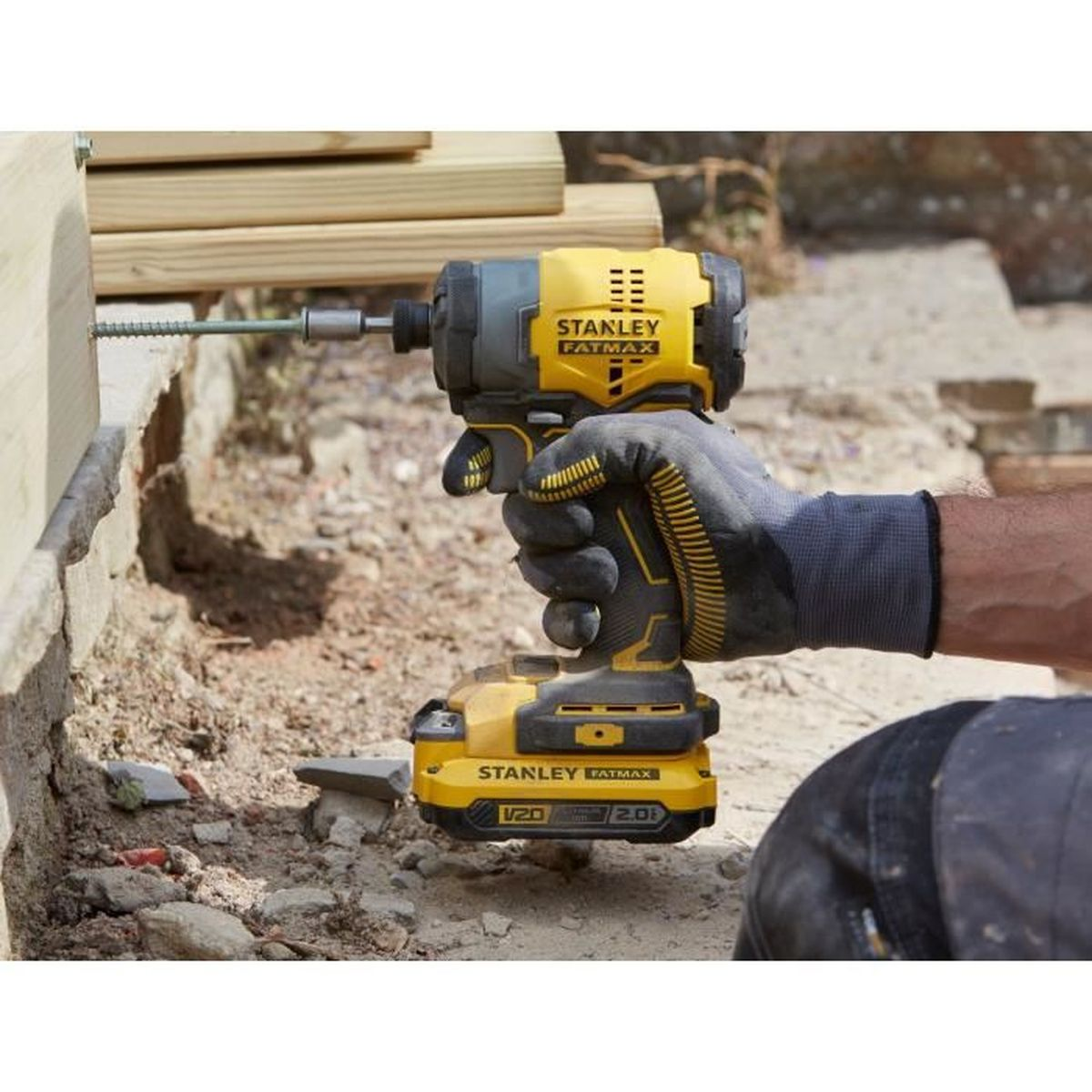 Una mano enguantada usa un atornillador de impacto amarillo Stanley Fatmax para atornillar en madera.
