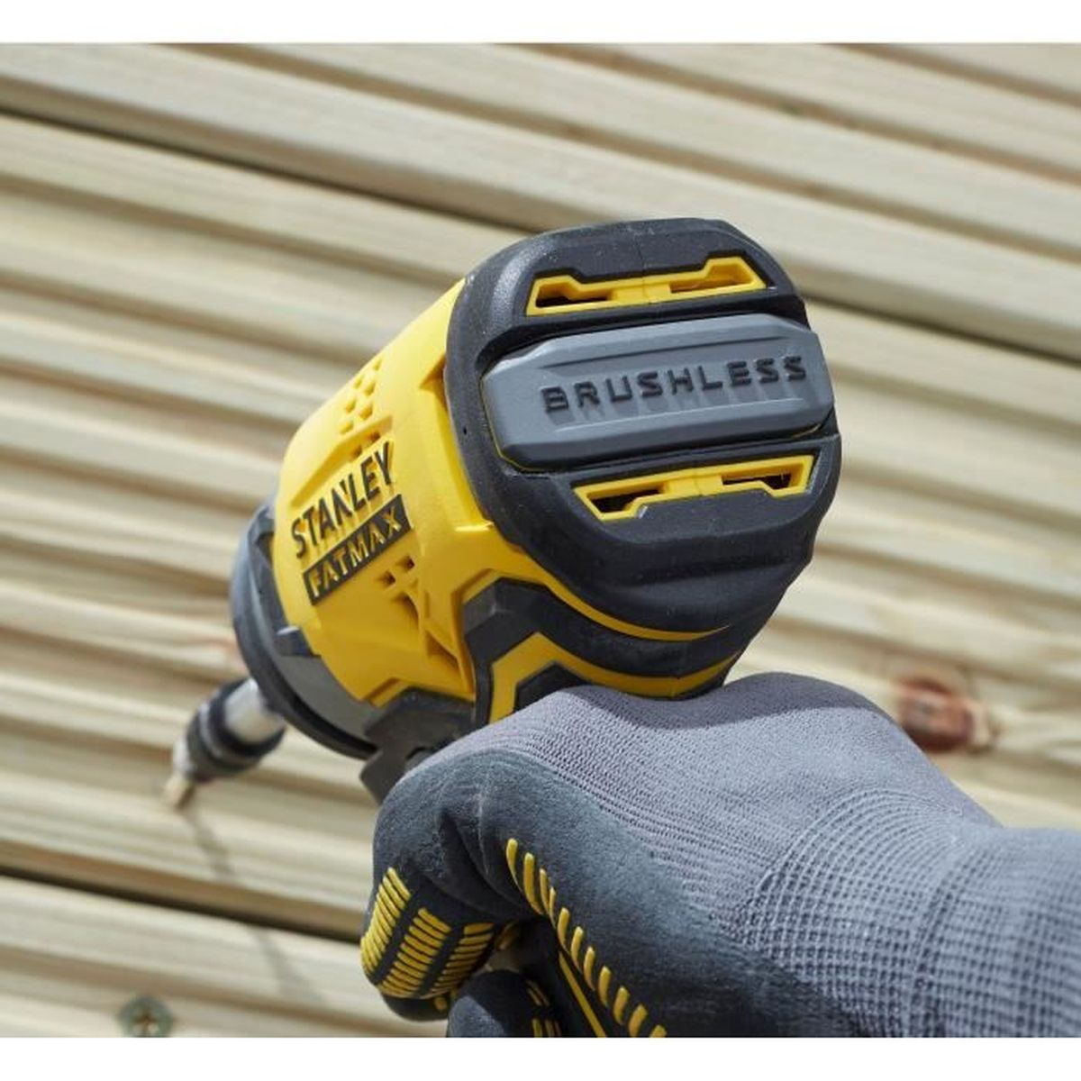 Una mano enguantada sostiene un taladro Stanley Fatmax sin escobillas amarillo atornillando tablones de madera.