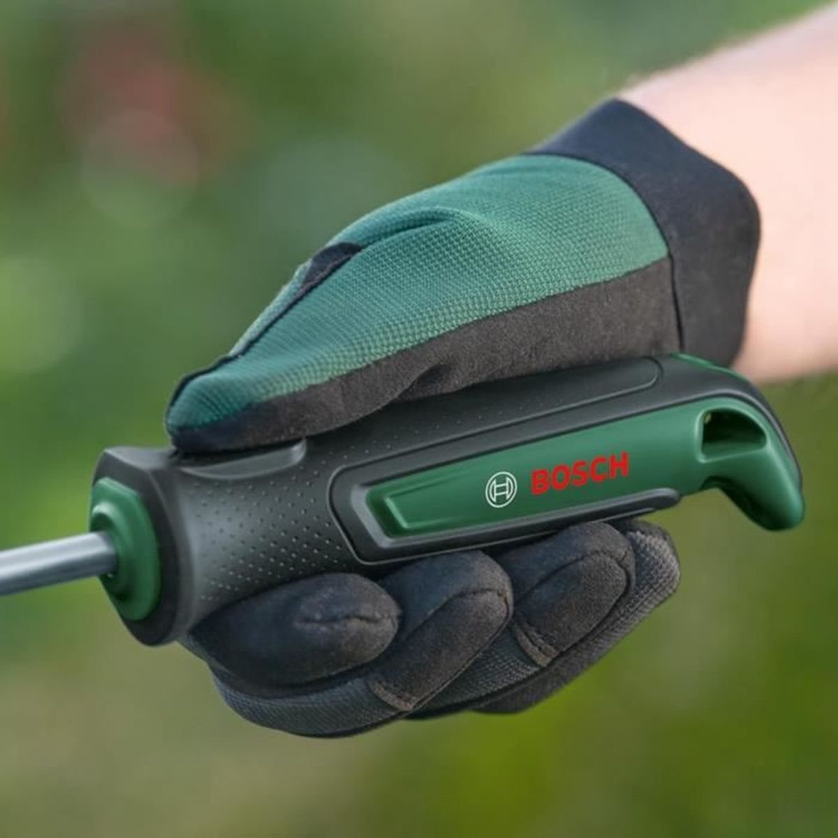 Yeşil bahçe eldivenleri, siyah bir Bosch bahçe aleti sapını tutuyor.