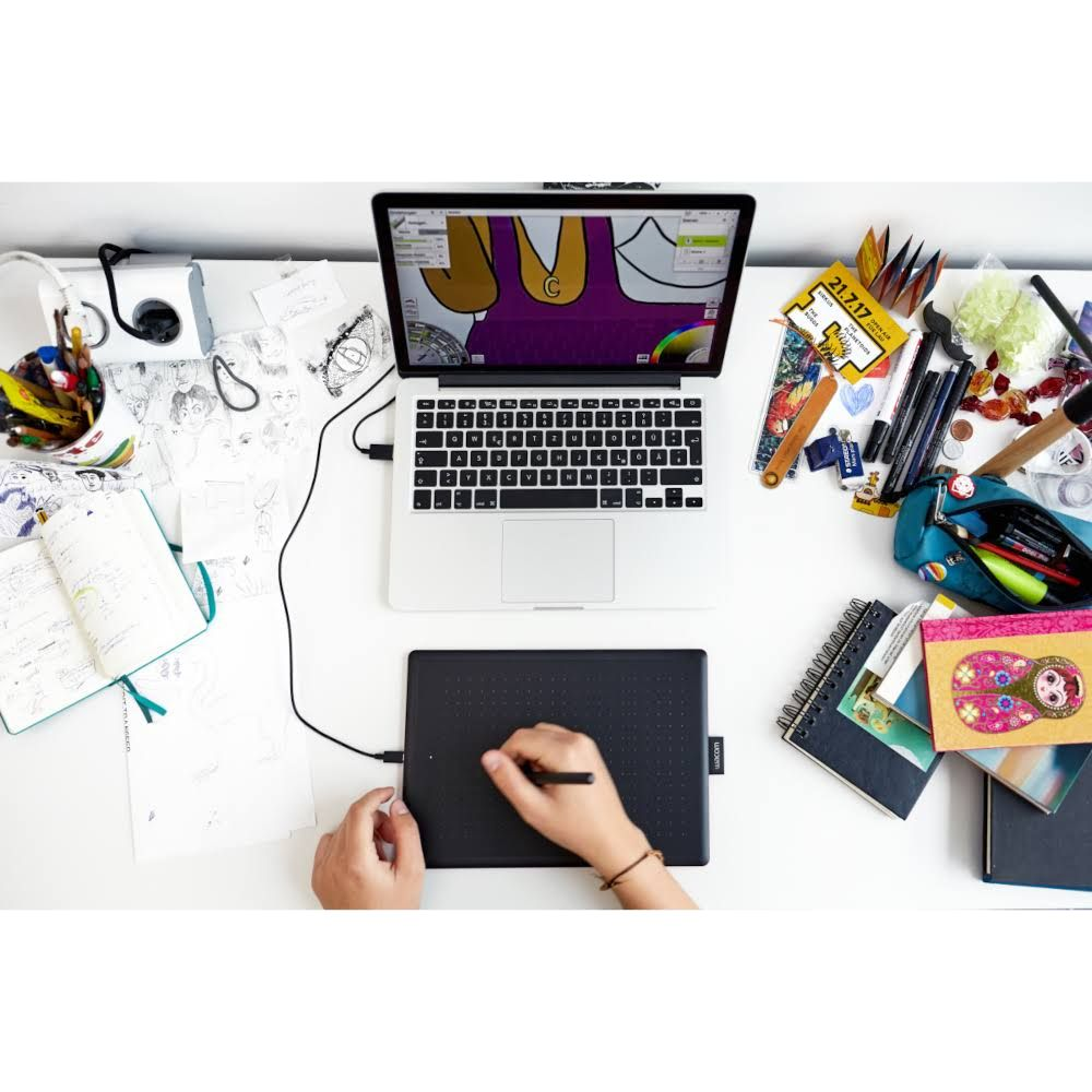 Una scrivania con laptop, tavoletta grafica e materiale artistico.