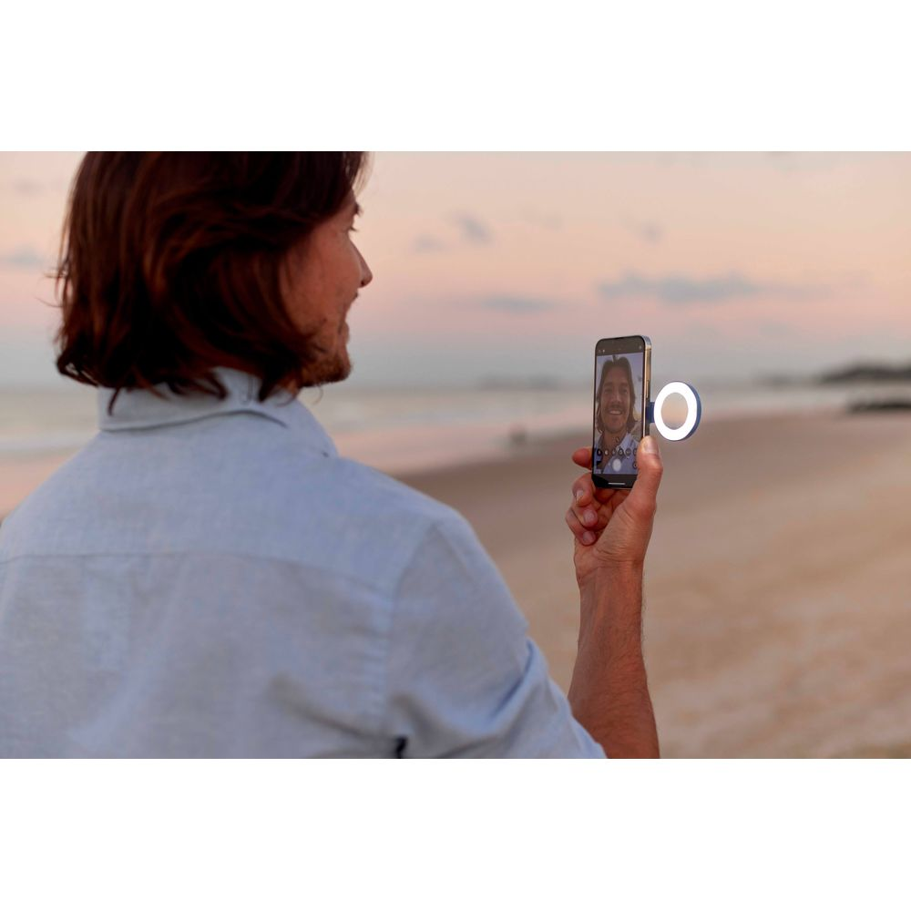 Homme sur la plage prend un selfie avec une lumière annulaire. Coucher de soleil, océan.