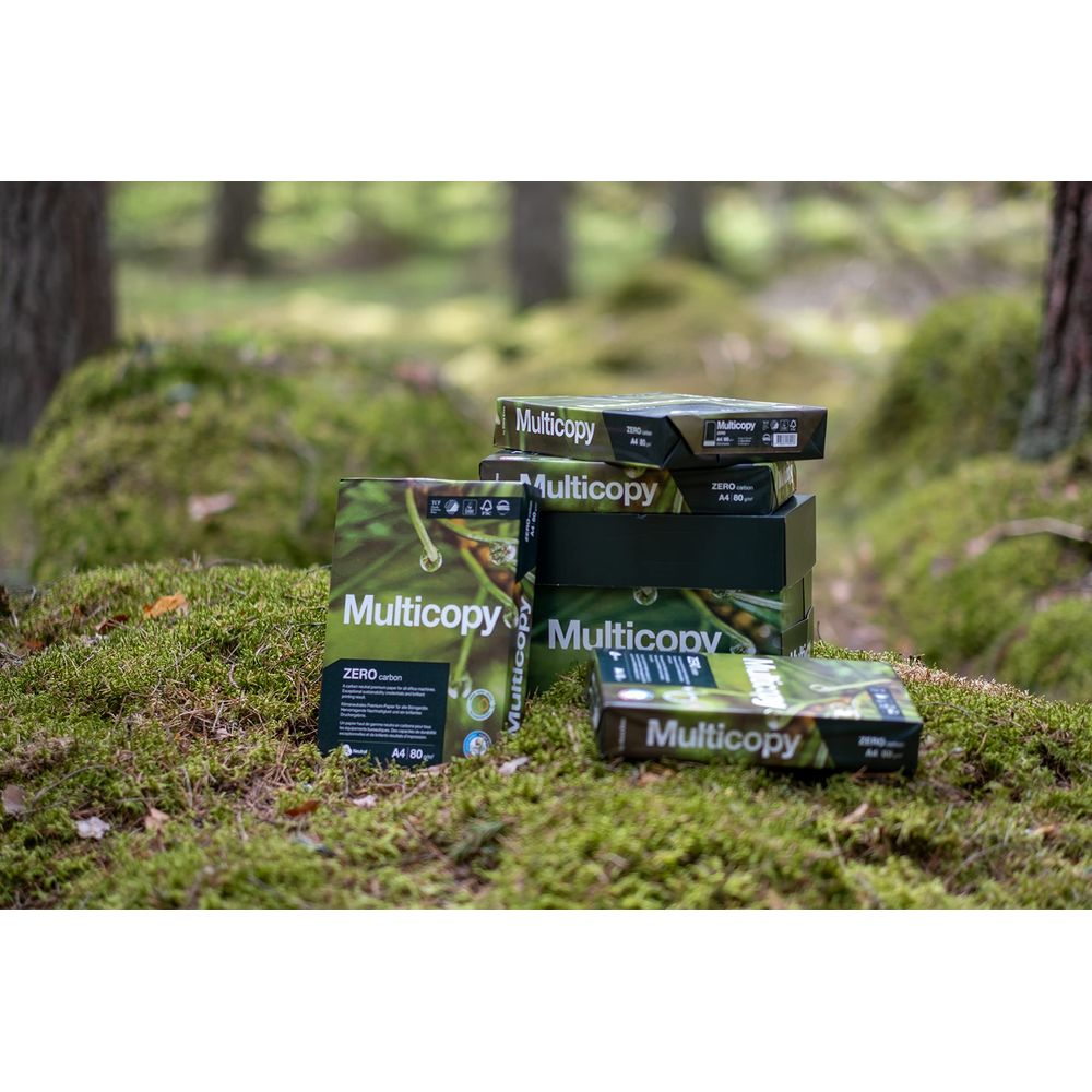 Kilka paczek papieru Multicopy leży na omszałej leśnej ziemi.