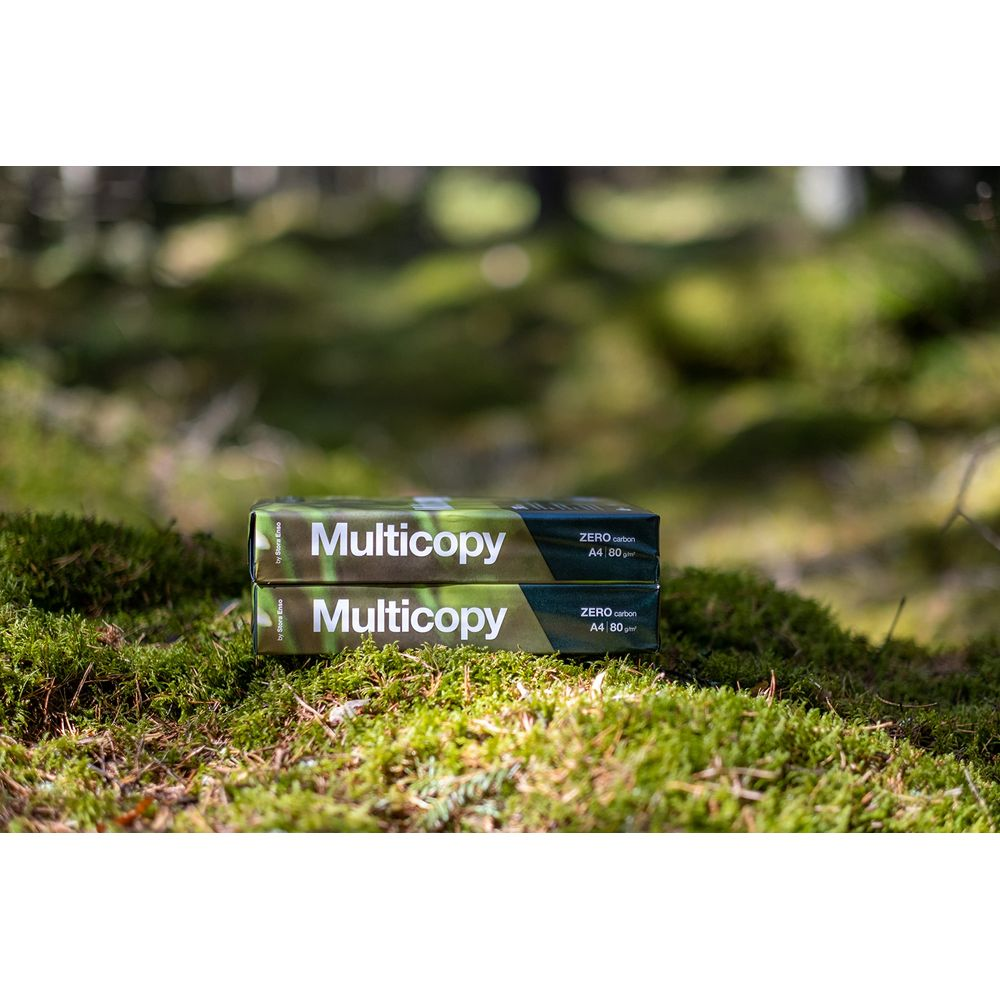 Dwa opakowania papieru Multicopy leżą na omszałej ziemi w lesie.