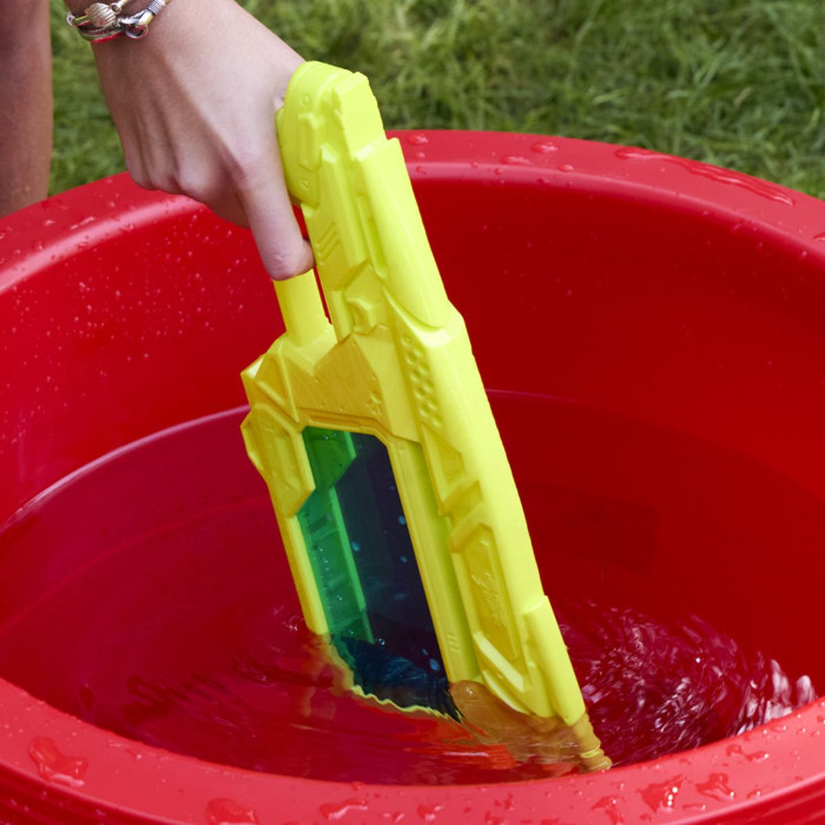 Eine Hand hält eine gelbe Wasserpistole in einem roten Eimer mit Wasser.
