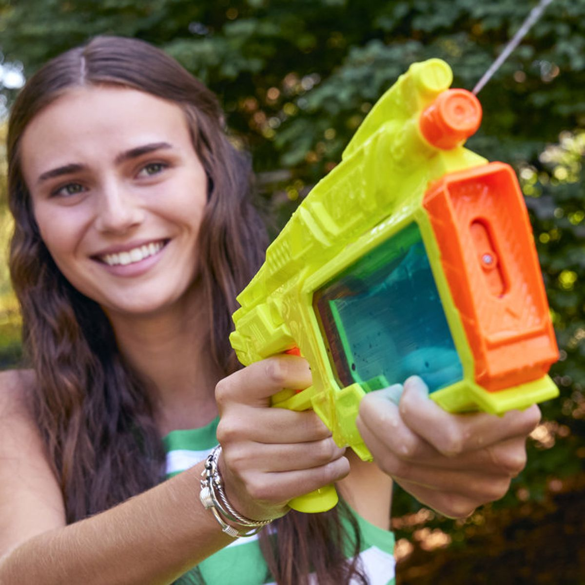 Ein junges Mädchen hält eine grüngelbe Wasserpistole mit orangefarbenen Akzenten.