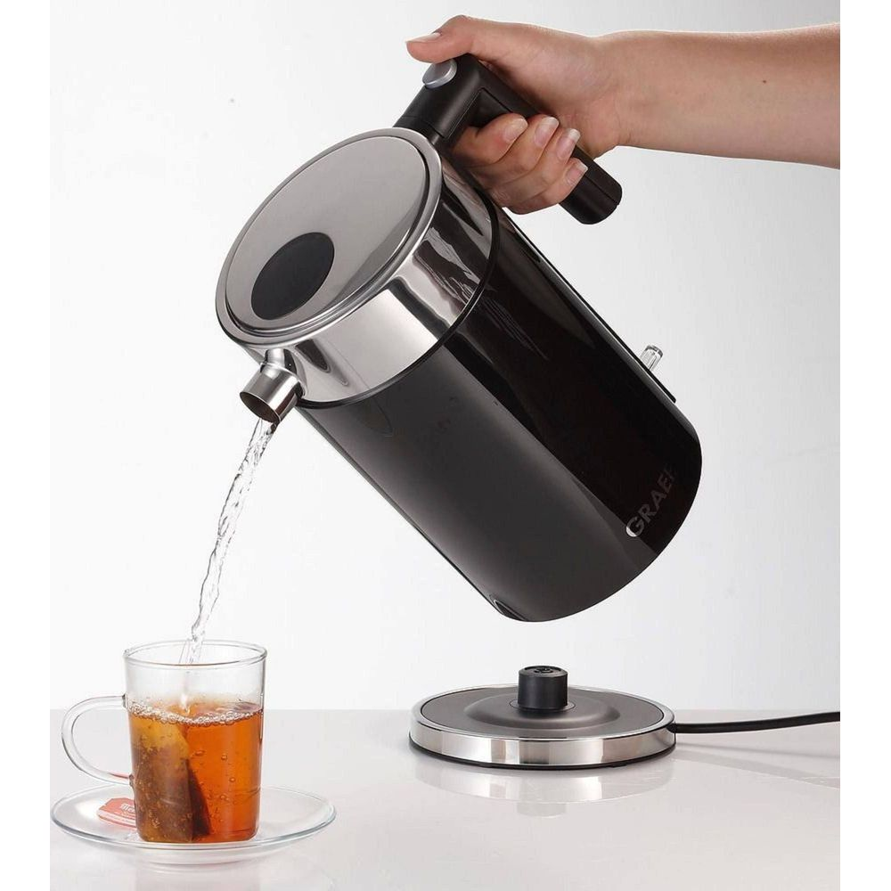 Eine Hand gießt Wasser aus einem schwarzen Wasserkocher in eine Teetasse.