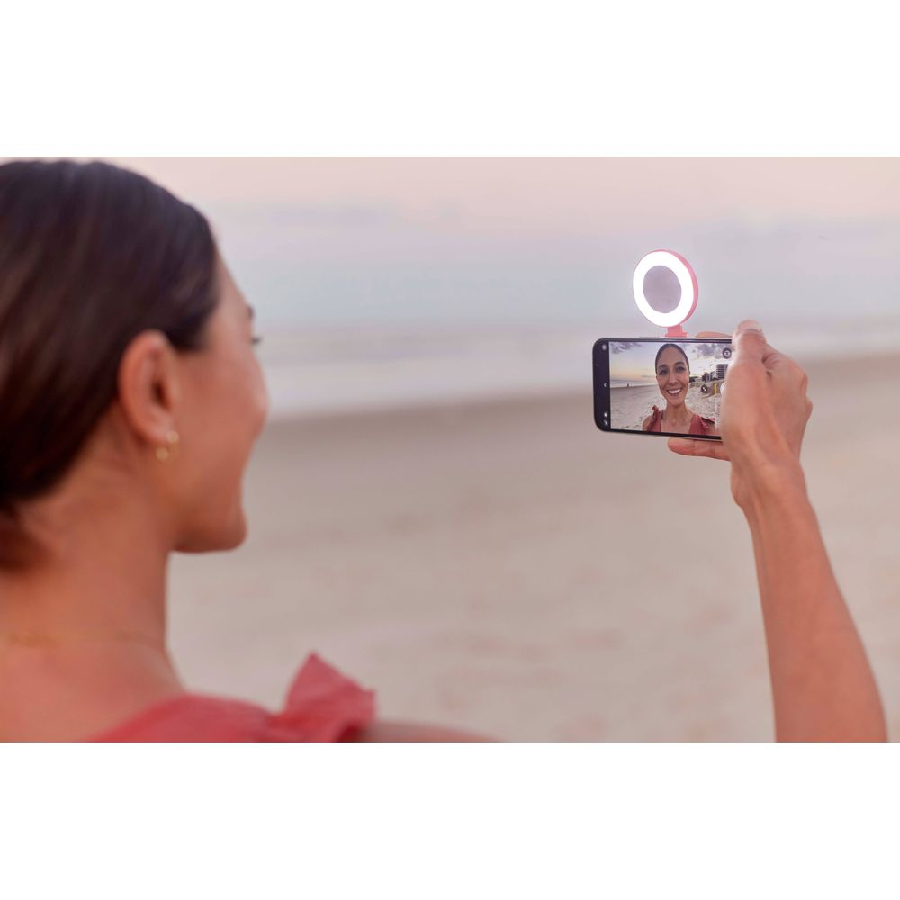Une femme sur la plage prend un selfie avec un téléphone à anneau lumineux.
