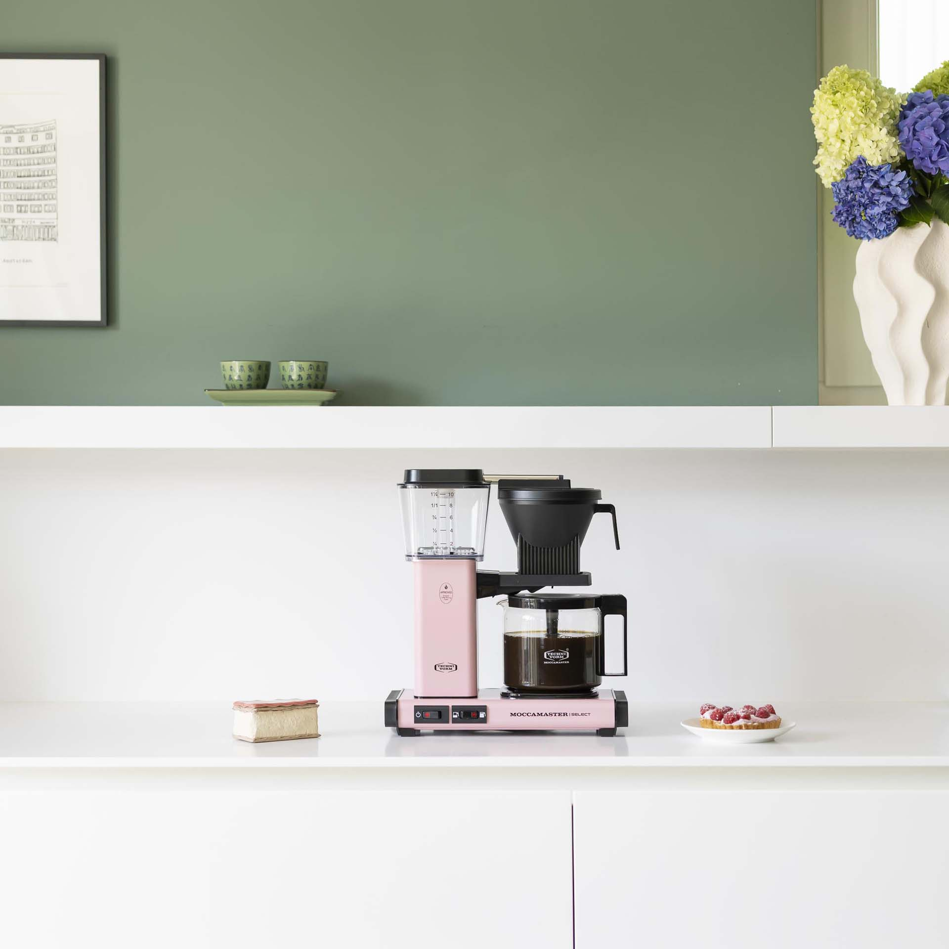 Eine rosa Kaffeemaschine steht auf einer weißen Arbeitsplatte mit einem Kuchen.
