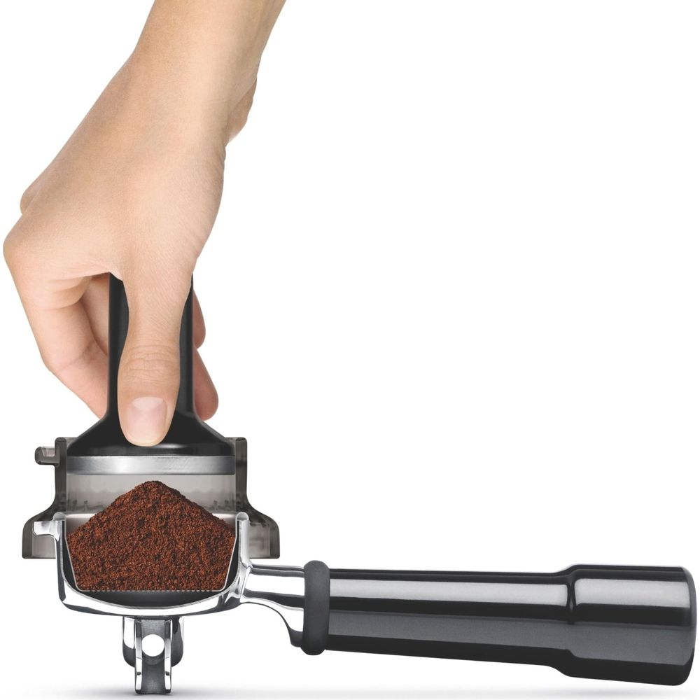 Une main tasse du café moulu dans un porte-filtre avec un tasseur.