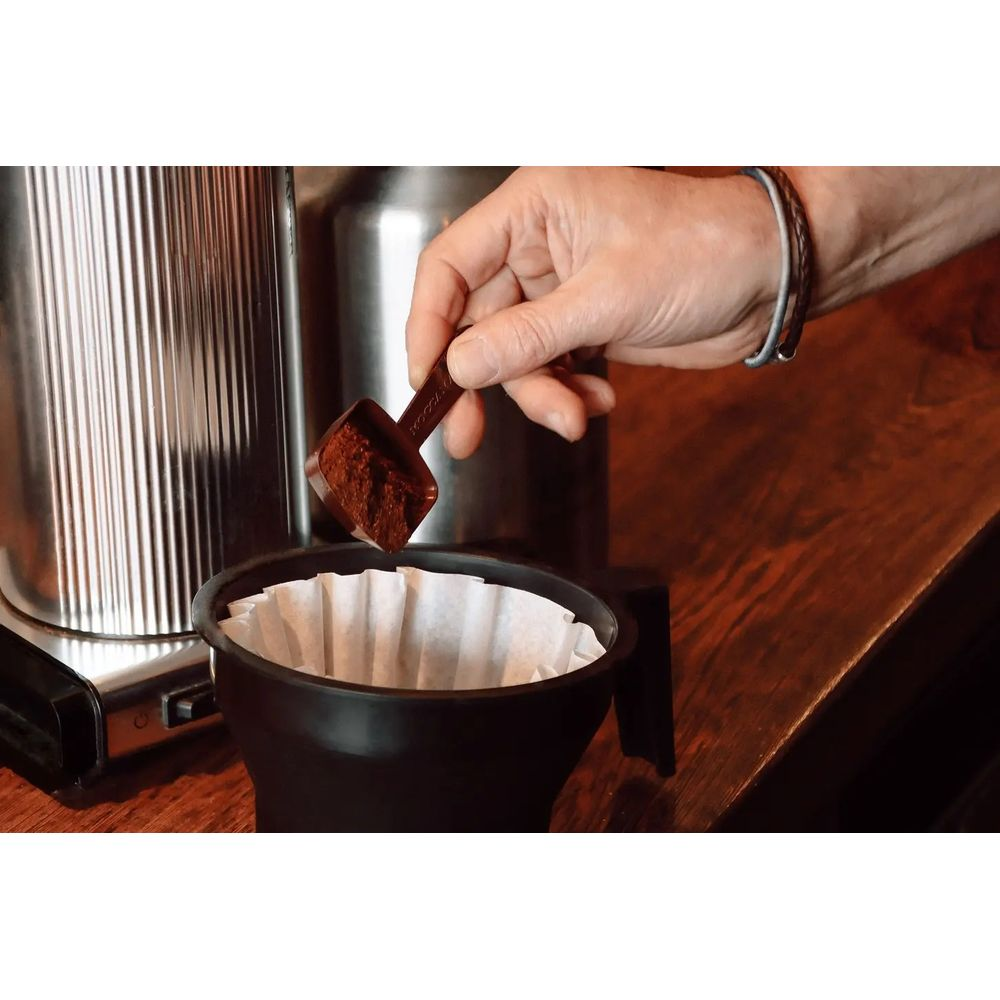 Una mano añade café molido a un filtro de café con una cuchara.